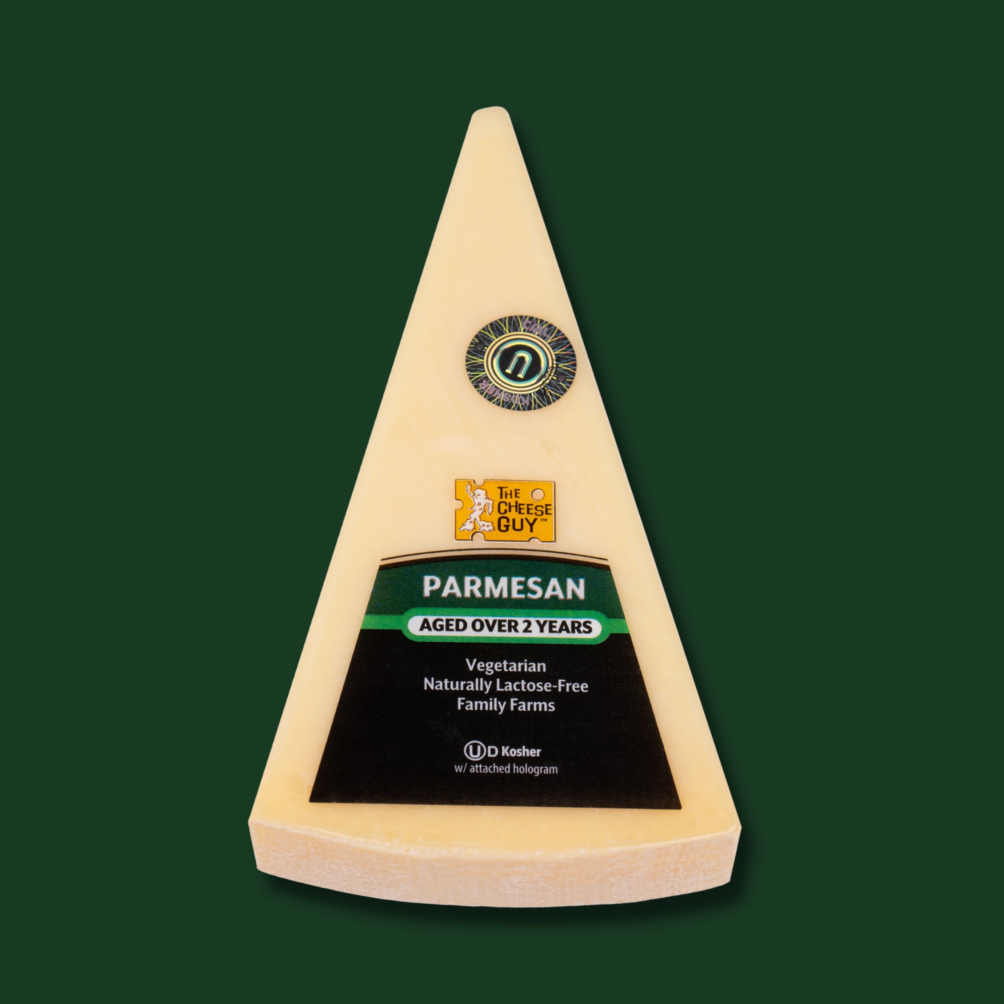 A wedge of The Cheese Guy 2 Year Aged Parmesan cheese, showcasing a dark label with the product name "PARMESAN" in green letters, clearly stating "AGED OVER 2 YEARS," and indicating it is vegetarian and naturally lactose-free, against a dark green background.