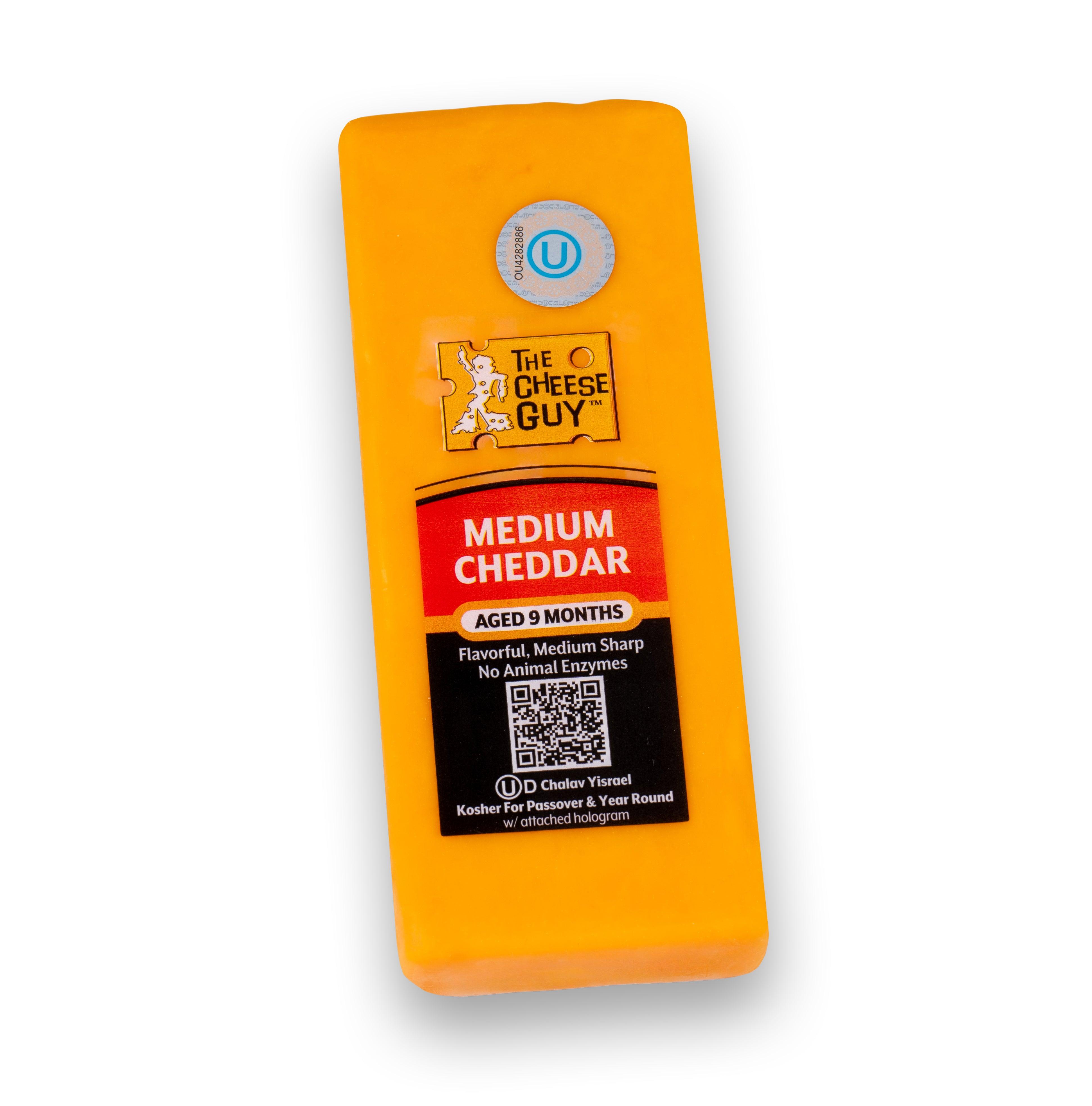 Image of The Cheese Guy Medium Cheddar, an orange rectangular block of cheese, showing the brand logo and 'Medium Cheddar' product name on the label, with 'Aged 9 Months' and 'No Animal Enzymes' details.