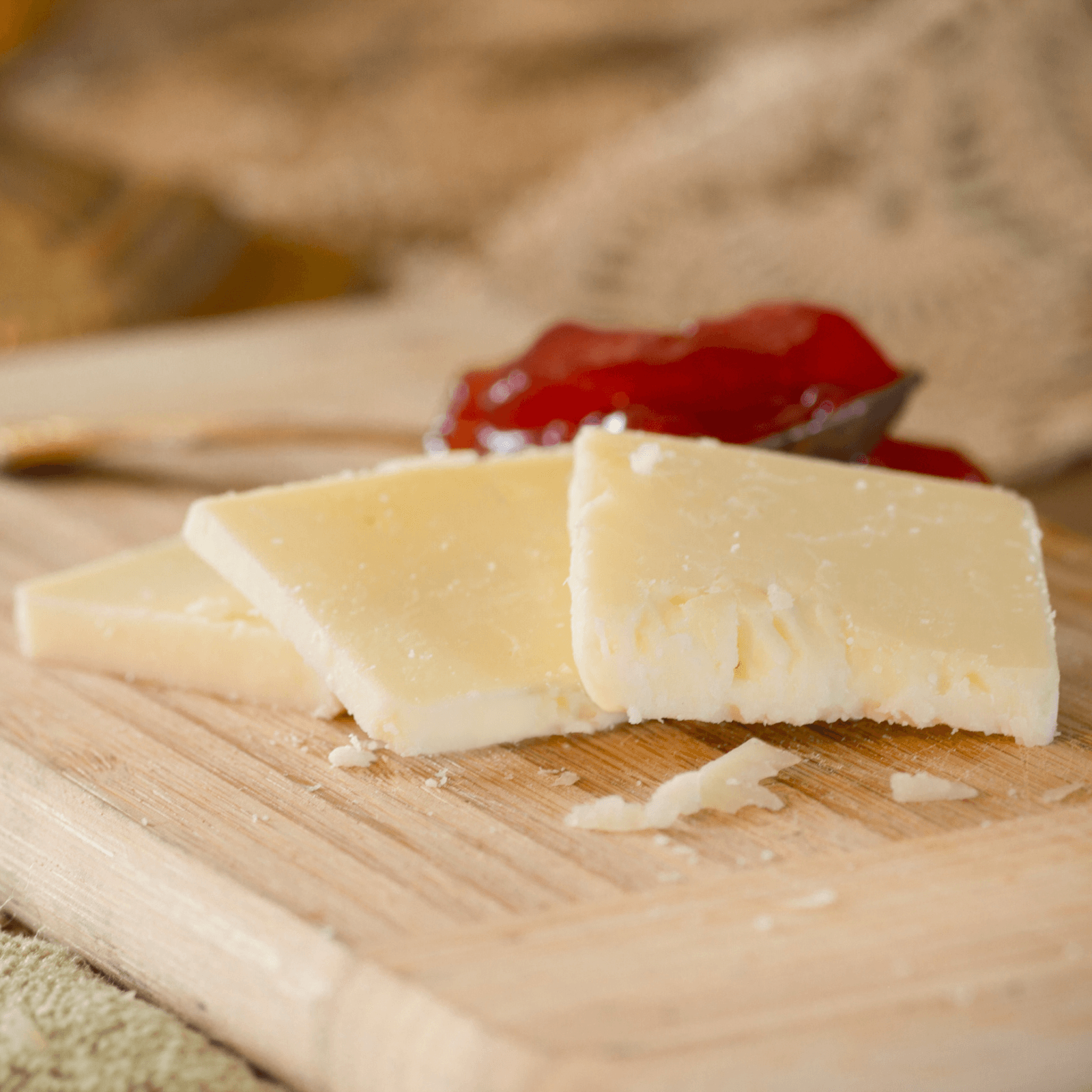 Three rectangular slices of pale yellow cheddar cheese arranged on a light brown wooden cutting board, topped with a dollop of red jam or chutney.