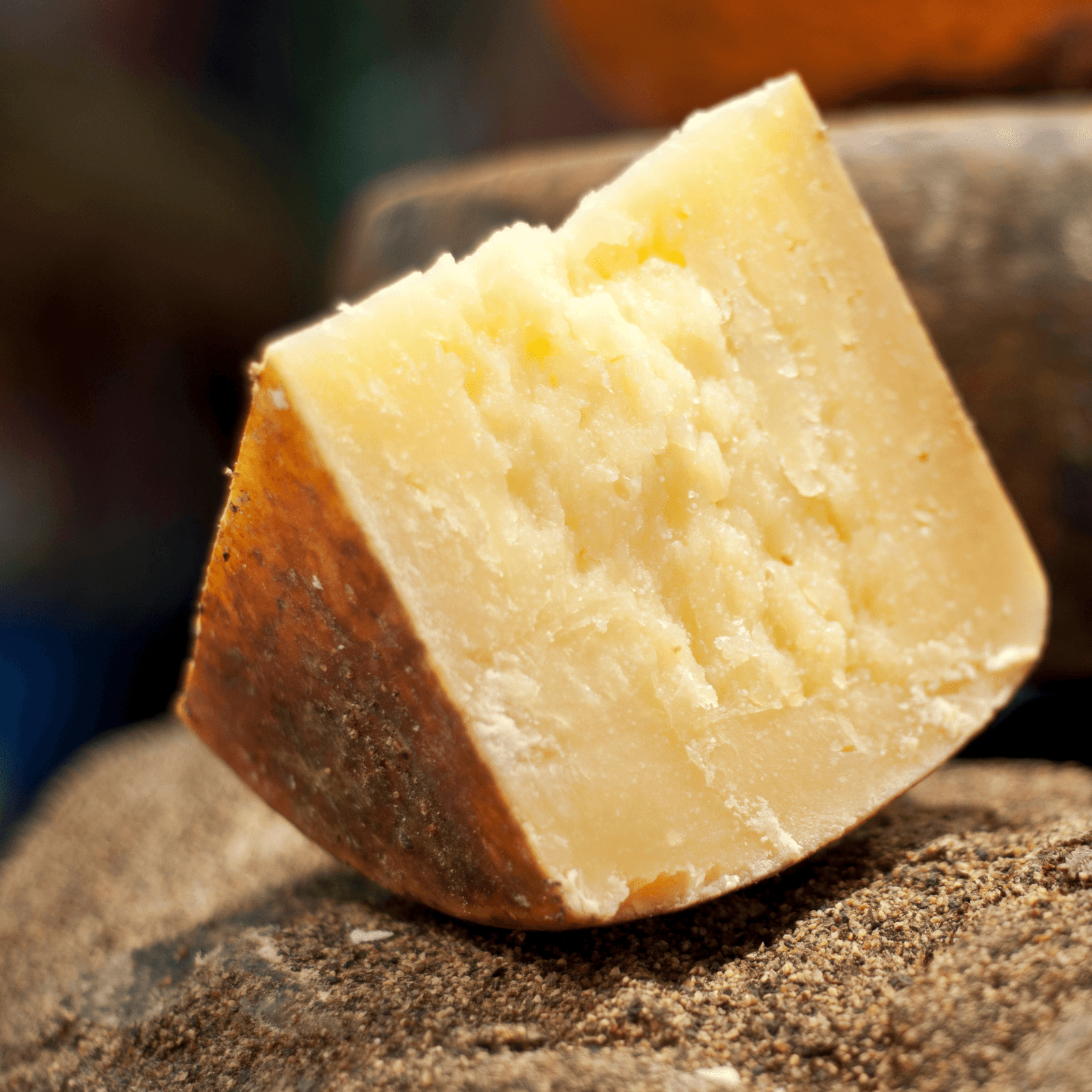 A triangular wedge of aged, hard cheese, likely Parmesan or Pecorino Romano, with a slightly darker rind resting on a rough, textured grey surface.