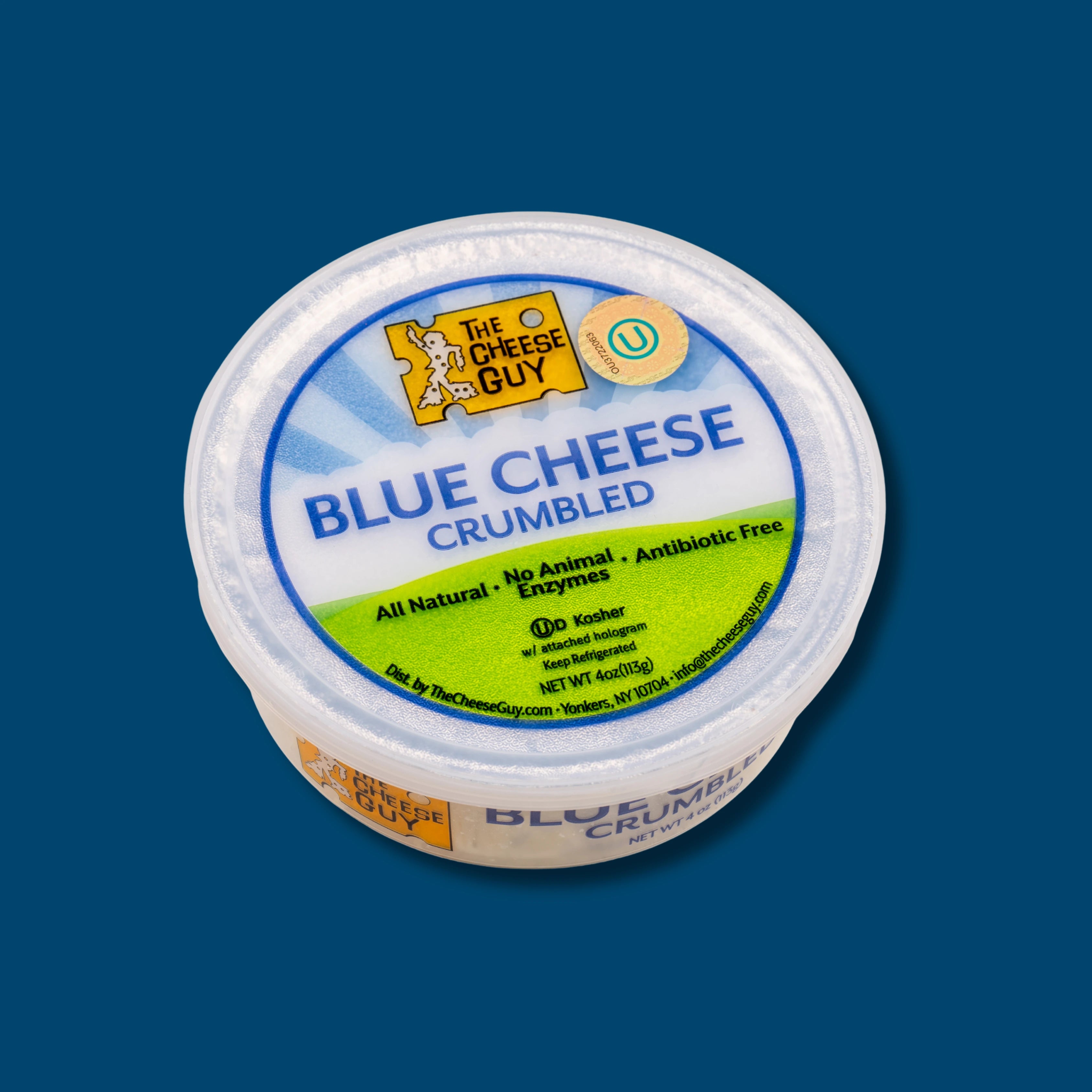 Image of The Cheese Guy Blue Cheese Crumbled, packaged in a round plastic container on a blue background, showing the brand logo, 'Blue Cheese Crumbled' product name, and attributes like 'All Natural' and 'Antibiotic Free'.