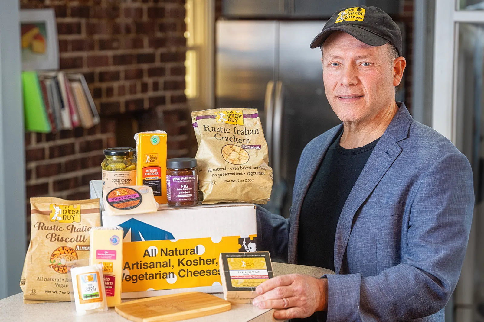Brent Delman with his products The Cheese Guy, featuring Rustic Italian Crackers, Rustic Magic Biscotti, and cheese. Text includes 'All Natural,' 'Artisanal,' 'Kosher,' and 'Vegetarian.