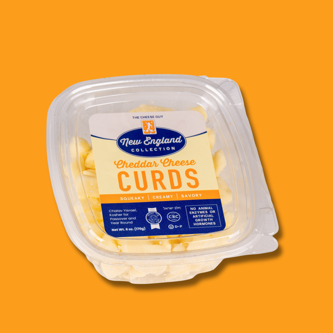 The Cheese Guy New England Collection Cheddar Cheese Curds in a clear plastic container with a blue and beige label emphasizing "Cheddar Cheese CURDS" and describing them as "Squeaky," "Creamy," and "Savory," against an orange background.