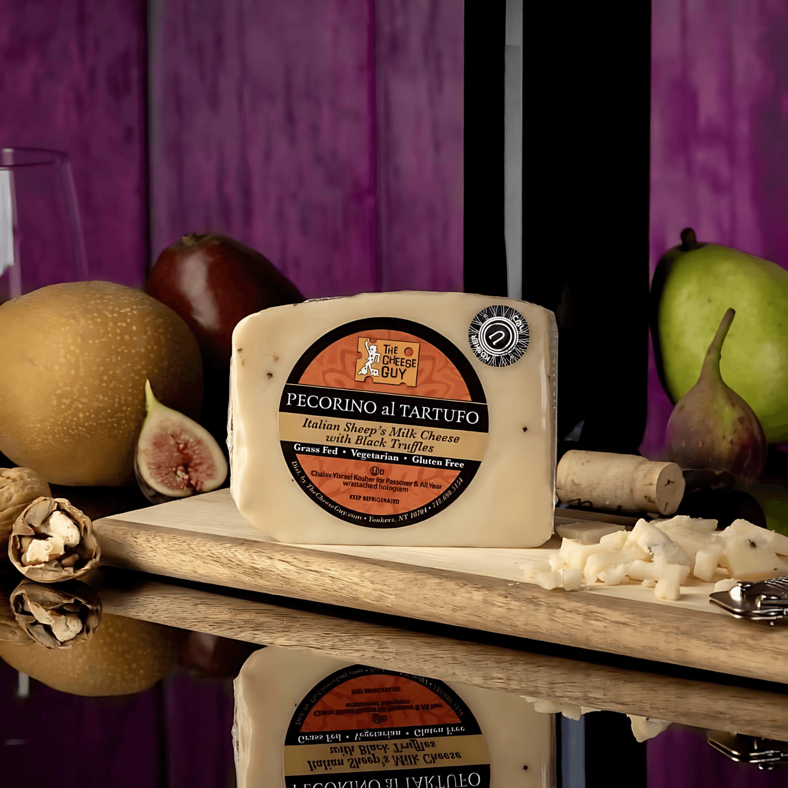 Image of The Cheese Guy Pecorino al Tartufo, an Italian sheep's milk cheese with black truffles, on a wooden serving board with pears, figs, and nuts, reflected on a glossy surface.